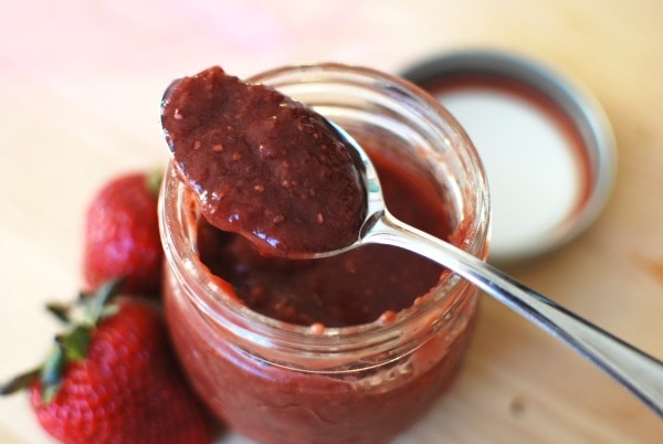 spoonful of homemade strawberry jam resting on a jar, on a wooden surface with strawberries