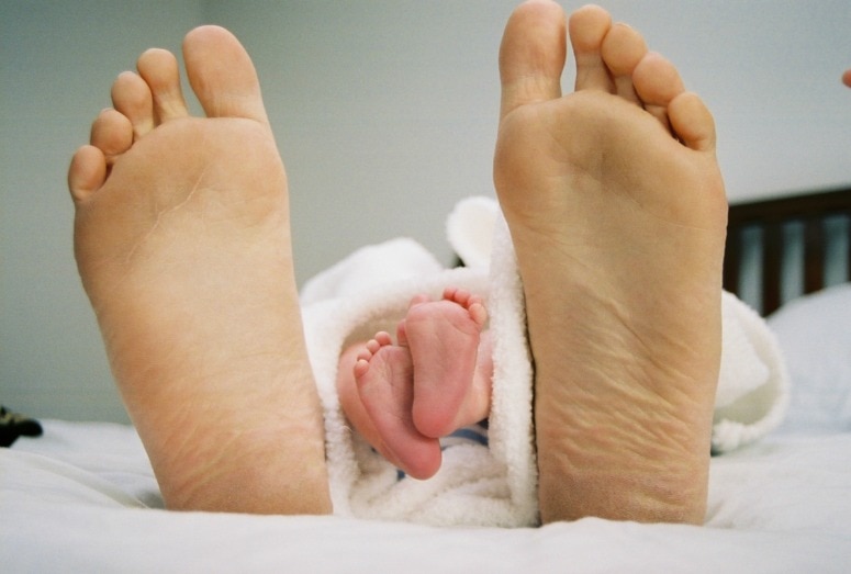 barefoot adult and baby feet on a bed