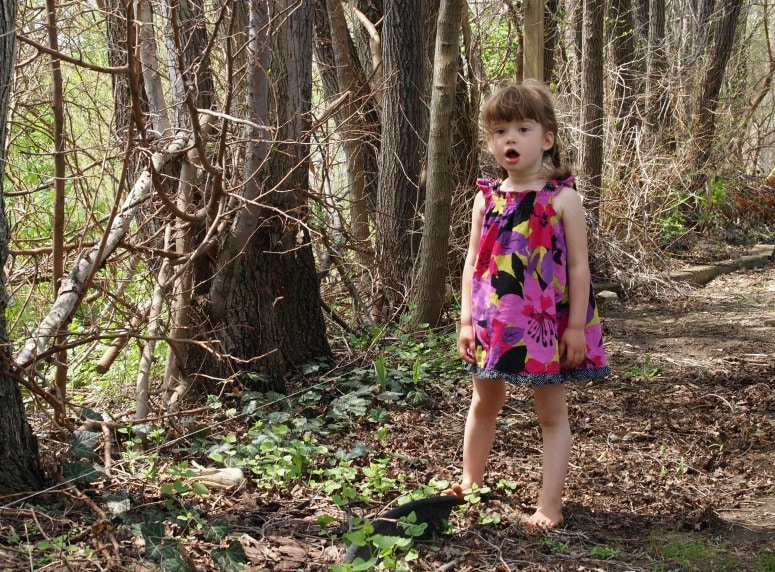 a little girl in a pink flower dress playing barefoot in a forested setting