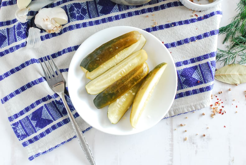 A photo from above, pickle spears sit on a white plate atop a blue and white tea towel. 
