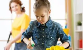 Image of a girl helping to keep the home clean by spraying a counter with cleaner and a cloth.
