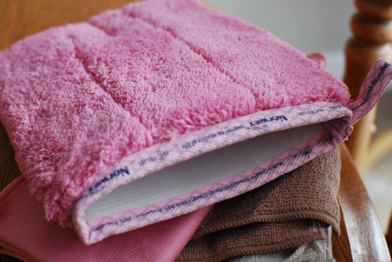 pink norwex scrub mitt on a stack of other norwex cloths