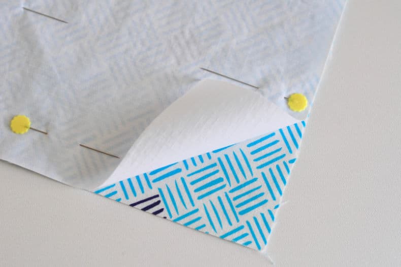 Fabric is pinned right sides together, the corner of the white nylon is lifted to show that the right sides have been pinned and shows the blue patterned fabric.