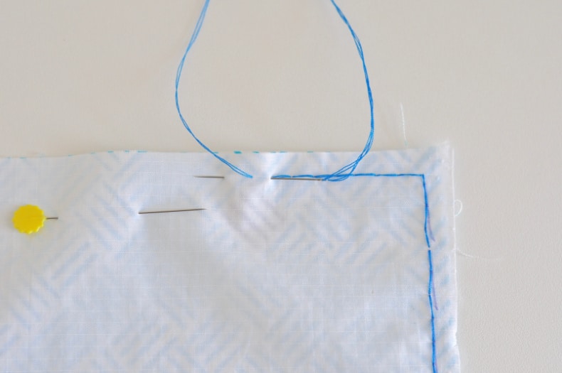 A needle and blue thread demonstrate the backstitch along the edge of the fabric being sewn together.