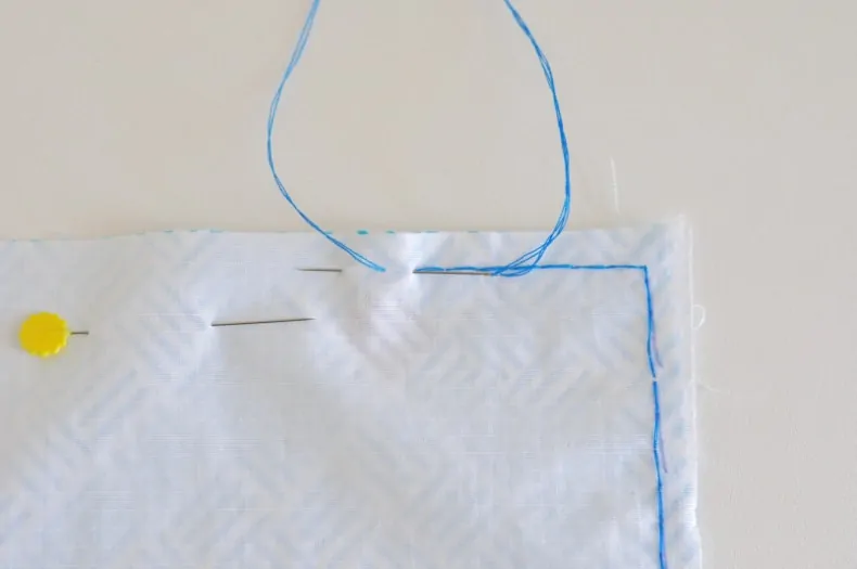 A needle and blue thread demonstrate the backstitch along the edge of the fabric being sewn together.