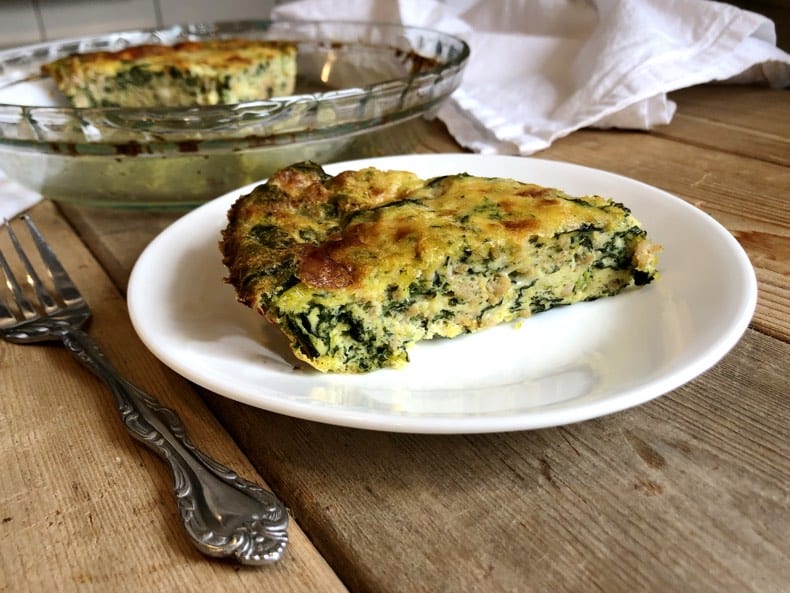 Image of sausage spinach frittata slice on a plate with white napkin and wooden background.