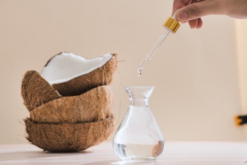 bottle of liquid coconut oil with hand taking dropper-full, next to a stack of coconut shells