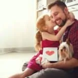 little girl kissing her dad's cheek with a greeting card and gift for dad