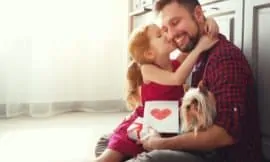 little girl kissing her dad's cheek with a greeting card and gift for dad