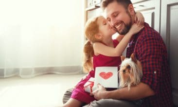 little girl kissing her dad's cheek with a greeting card and gift for dad