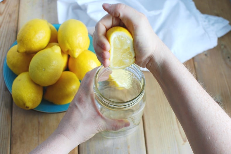 hands juicing a lemon by squeezing into a jar