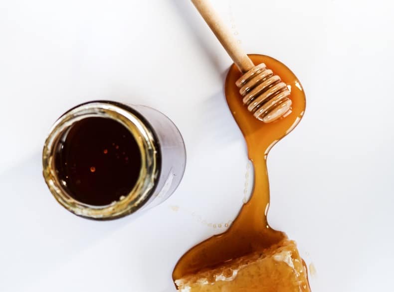 honey stick on white surface with honey drips and jar of honey