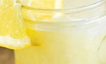 close up image of homemade lemonade in a pint jar, with a slice of lemon on the rim of the cup