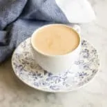 Butter Chai Latte in a white teacup sits on a blue and white saucer on a marble counter. A blue tea towel sits in the background.