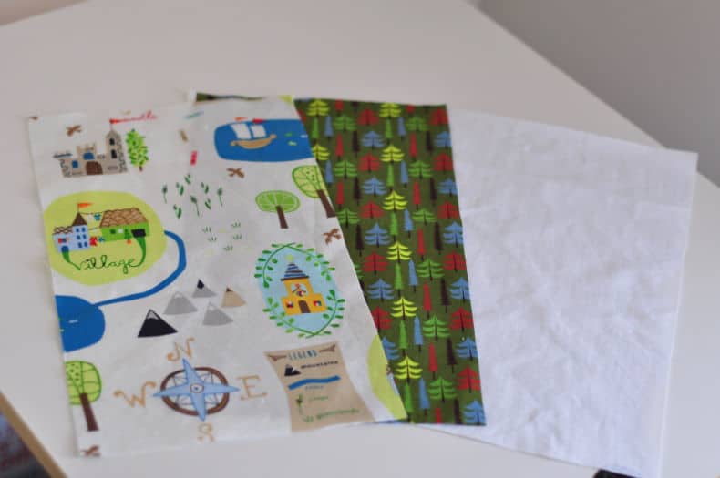 Coordinating adventure/woodland themed green and blue cotton fabric and white nylon, cut to size, is laid out on a white surface.