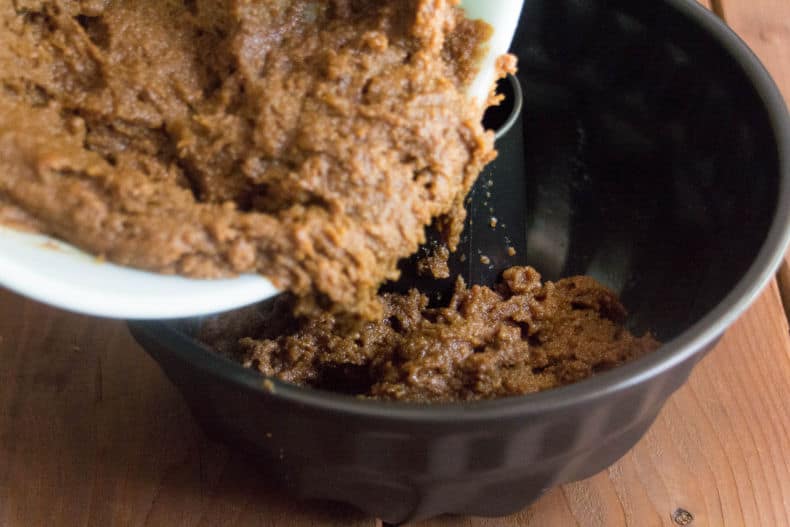 Honey mixture and dry ingredients have been combined and are poured into a black greased bundt cake pan.