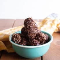 A teal bowl with a pyramid of chocolate macaroons sits on a brown wood table with a yellow tea towel deoratively placed in the background.