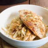 A white bowl with a bed of cabbage noodles and a chicken breast on top.