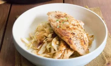 A white bowl with a bed of cabbage noodles and a chicken breast on top.