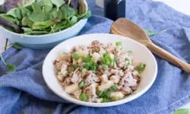 Waldorf Tuna Salad in a white bowl, on top of a blue tea towel. A bowl of baby spinach sits in the background, a wooden spoon sits nearby.