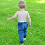 Baby wearing navy and bright blue striped upcycled sweater pants walks on green grass.