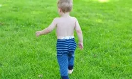 Baby wearing navy and bright blue striped upcycled sweater pants walks on green grass.