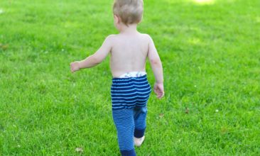 Baby wearing navy and bright blue striped upcycled sweater pants walks on green grass.