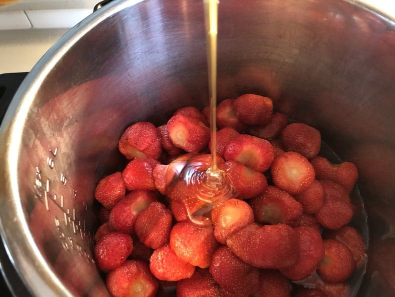 making homemade strawberry jam - pouring honey over strawberries in the instant pot