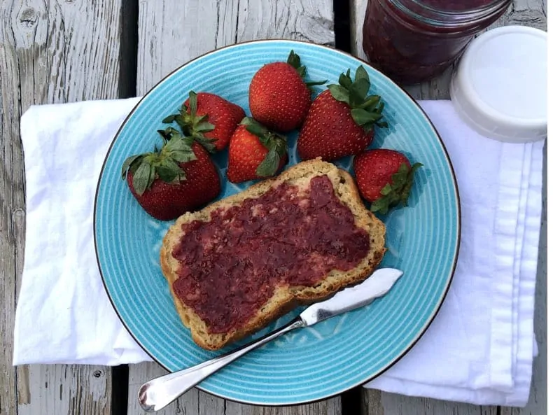 homemade strawberry jam on bread, on a plate with strawberries and a white napkin underneath