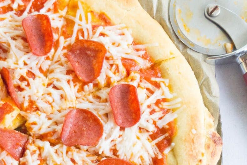 close-up shot of paleo pizza crust with pepperoni and cheese toppings, with a pizza cutter