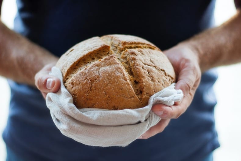 Image is of a person holding out a loaf of fresh bread.