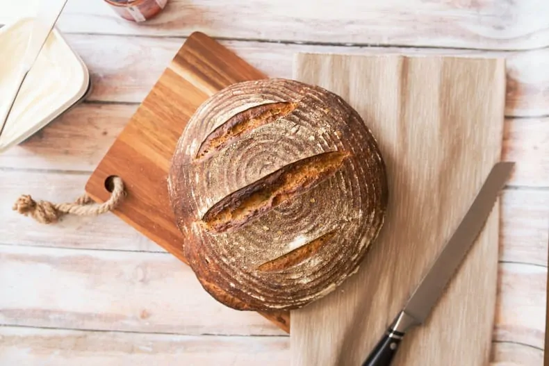Image is of a loaf of sourdough bread on a cutting board with a knife.