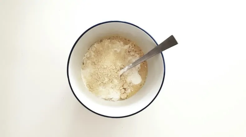 Image is of a bowl with bread ingredients partially mixed in it, and a utensil resting on the side.