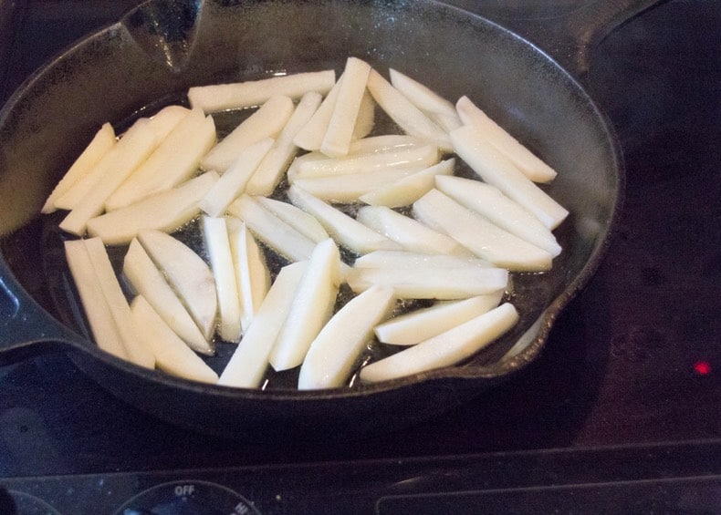 Homemade french fries cut up and frying in a cast-iron pan.