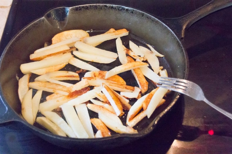 Homemade french fries cut up and cooking in a cast iron pan, almost golden brown.