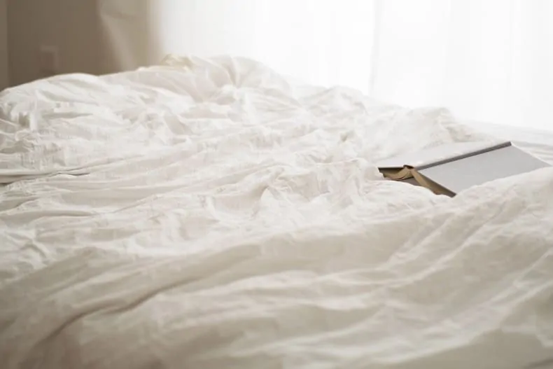 Bed with white duvet and a book lying on it.