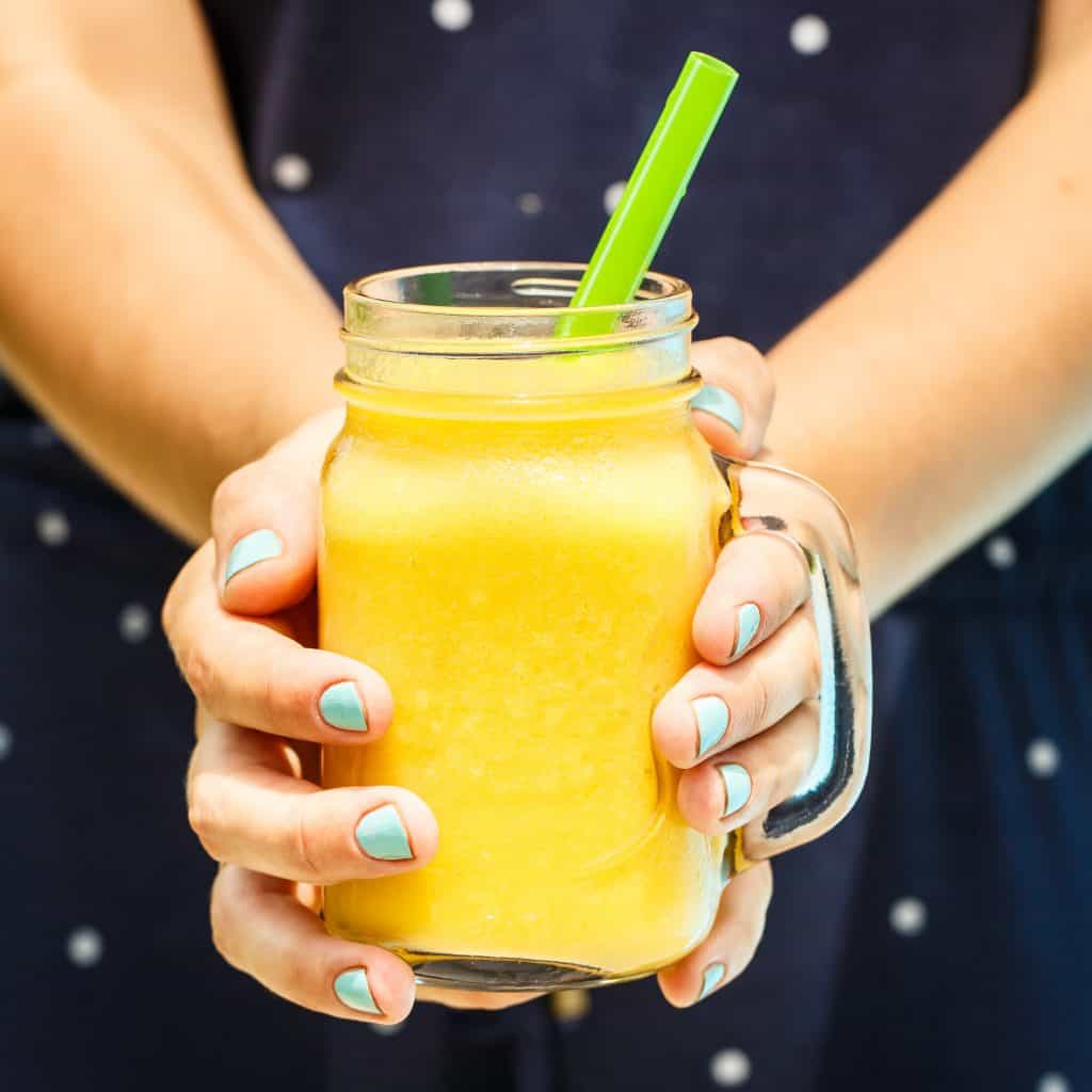 close up shot of hands holding a cold fruity drink with a green straw
