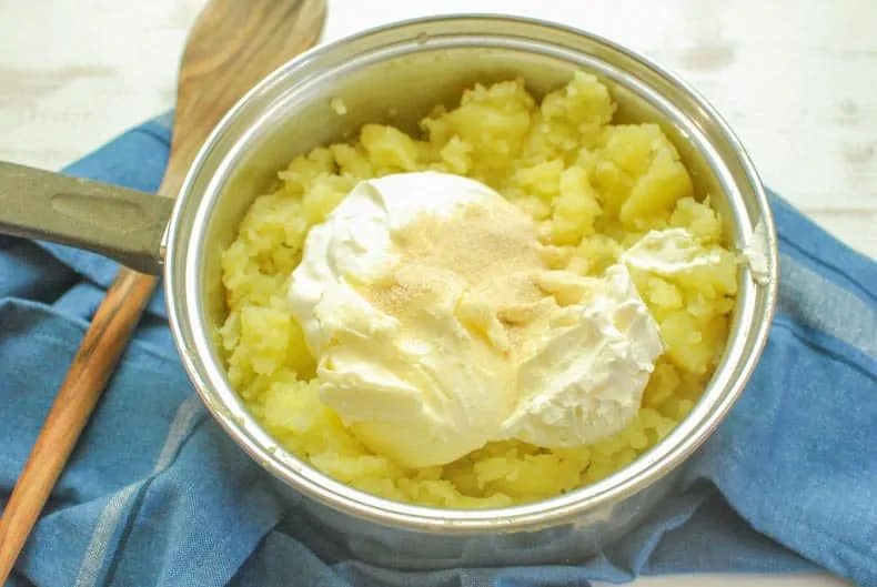 Pot of boiled and smashed potatoes with sour cream, cream cheese, and seasonings waiting to be mixed.