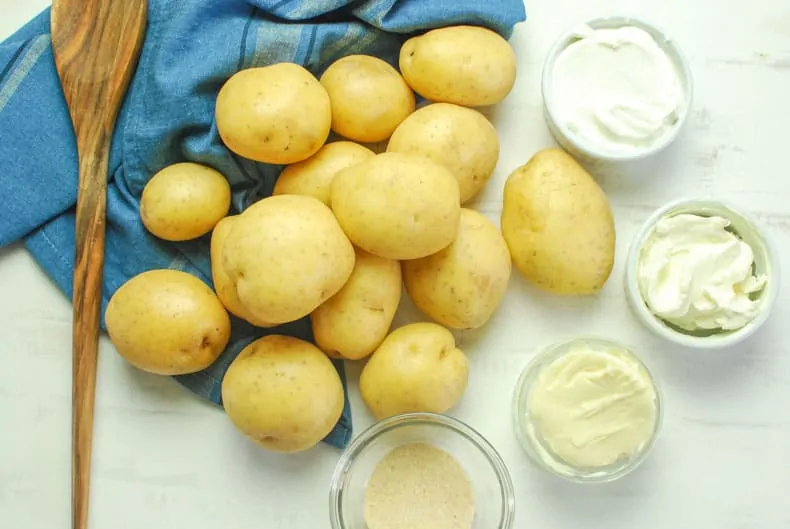Ingredients for sour cream mashed potatoes with a blue towel and wooden spoon.