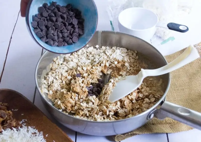 Granola bar ingredients being put together: chocolate chips pouring into dish with oats and nut butter.