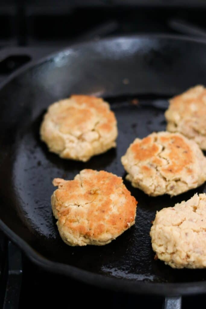 gluten free salmon patties frying in a cast iron skillet with coconut oil