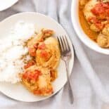 plate of instant pot curry chicken with rice, plus a bowl of chicken for serving, on a grey linen