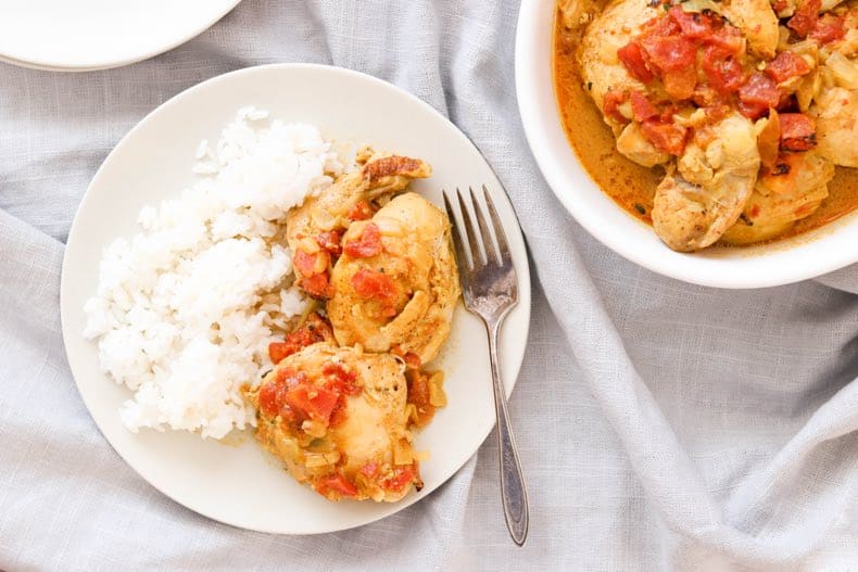 plate of instant pot curry chicken with rice, plus a bowl of chicken for serving, on a grey linen 