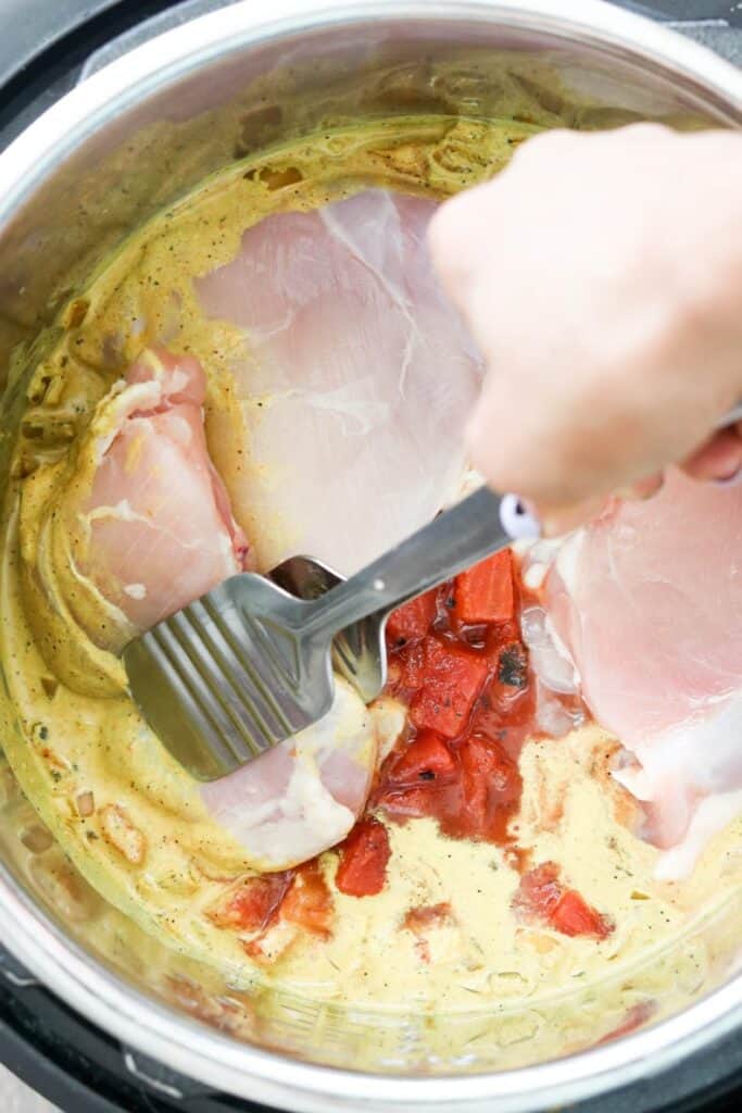 close up of raw chicken added to instant pot with curry ingredients to stir and cook (coconut milk, tomatoes, etc.)