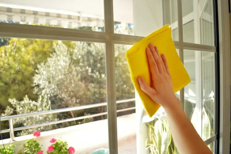 an arm and hand holding a yellow cloth, spring cleaning a window from inside an apartment