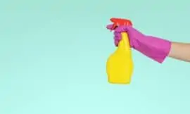 a blue background with a pink-gloved arm holding out a yellow spray bottle for spring cleaning
