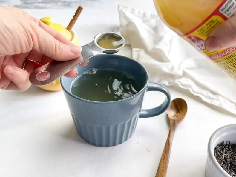 adding a teaspoon of apple cider vinegar to a mug of tea remedy made with ginger and green tea and lemon