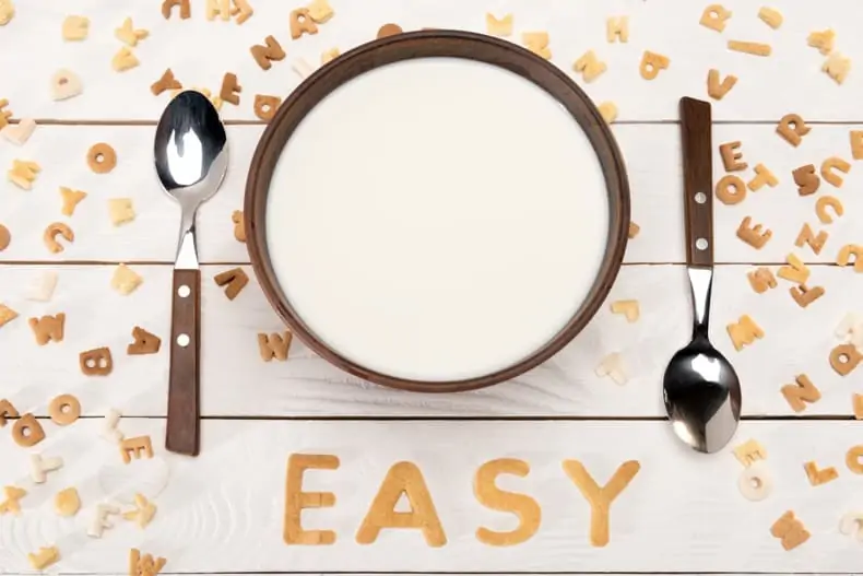 a bowl of milk with alphabet cereal around it, some spelling out the word EASY
