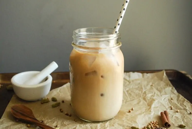 A straight-on shot of the chai latte with ice in the cup, a paper straw, and dark surface and background.
