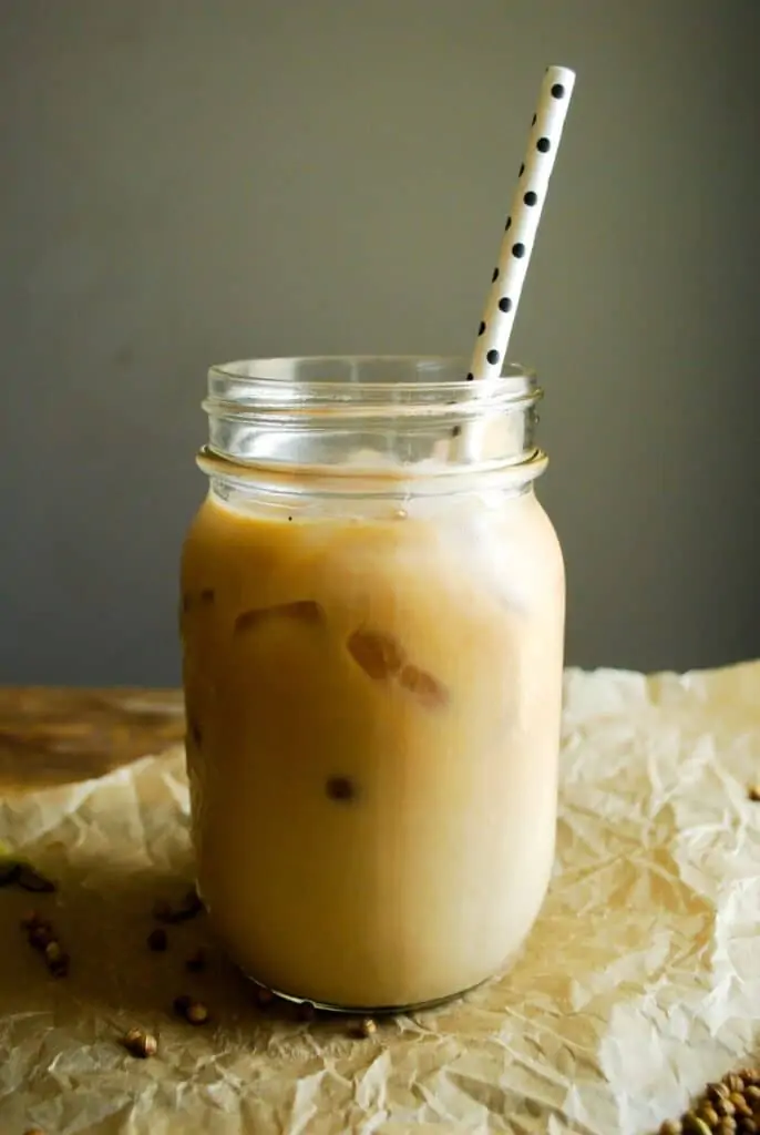 a straight-on shot of a mason jar glass of iced chai tea latte with a wood surface, dark background, and black and white polka dot paper straw.